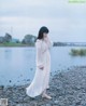 A woman in a white dress standing on a rocky beach.