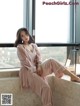 A woman sitting on a window sill in a pink robe.